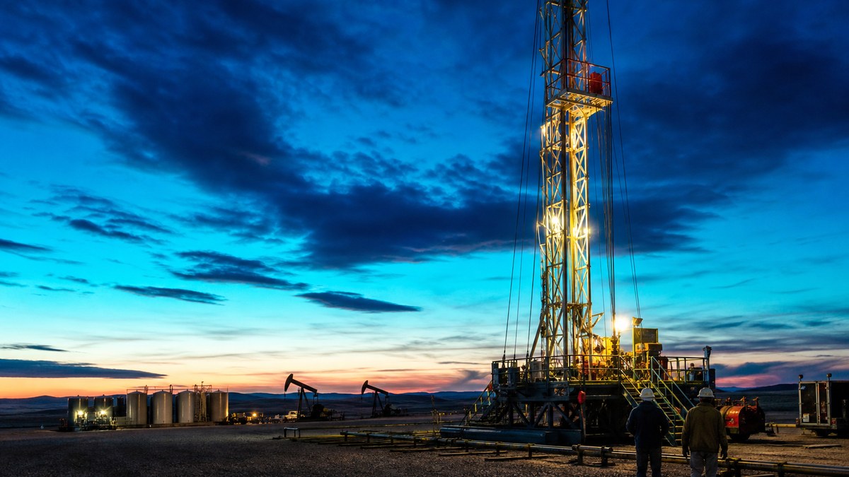 Workover rig servicing a producing well on a Bakken well pad at dusk, North Dakota
